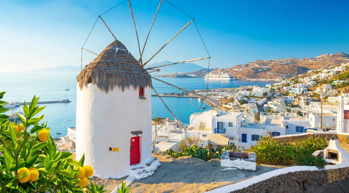 Peisaj din Mykonos, Grecia. O căsuță cu o elice în fata ei. În fundal se văd mai multe plaje și apa
