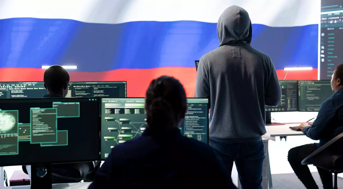 Imagine cu mai mulți hackeri ruși aflați în fața calculatoarelor. Unul stă în picioare, uitându-se la un ecran care afișează steagul Rusiei