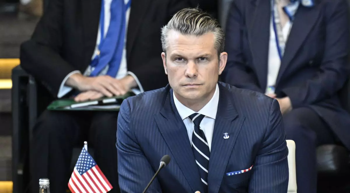 Șeful Pentagonului, Pete Hegseth, îmbrăcat la costum gri, ascultă în fața unui laptop și a unui steguleț al SUA, declarațiile altor reprezentanți la summit-ul NATo din iunie 2025