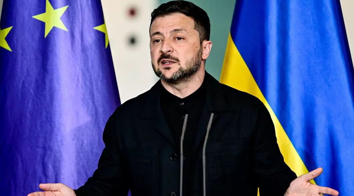 Volodimir Zelenski, îmbrăcat într-o cămașă neagră, dă explicații cu mâinile larg deschise în timpul unei conferințe de presă, având în spate steagurile Ucrainei și al Uniunii Europene
