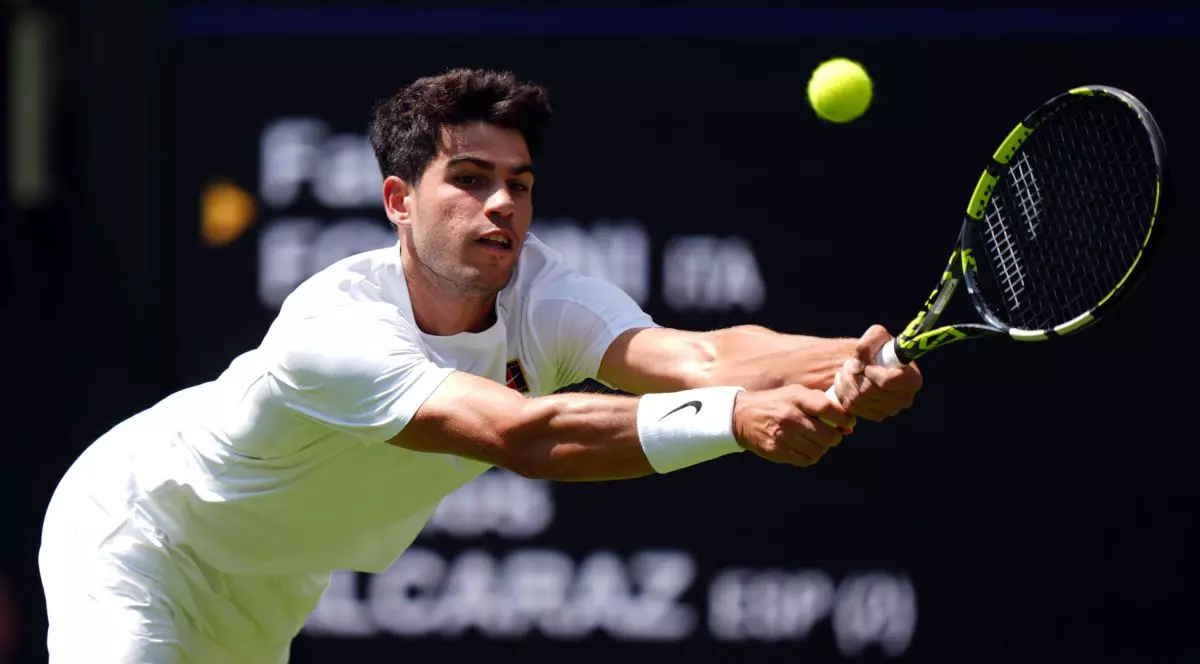 Carlos Alcaraz, îmbrăcat în alb, se întinde și returnează o minge în timpul unei partide de la Wimbledon, iunie 2025
