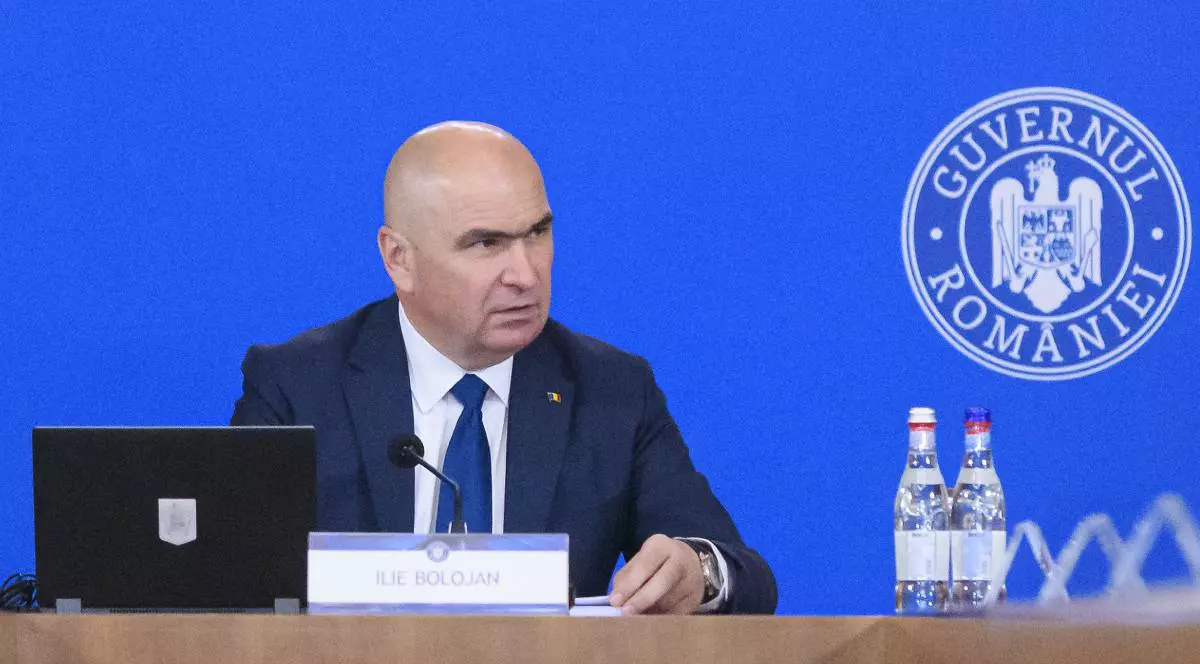 Ilie Bolojan la începutul ședinței de guvern, este îmbrăcat în costum și se uită în partea stângă.