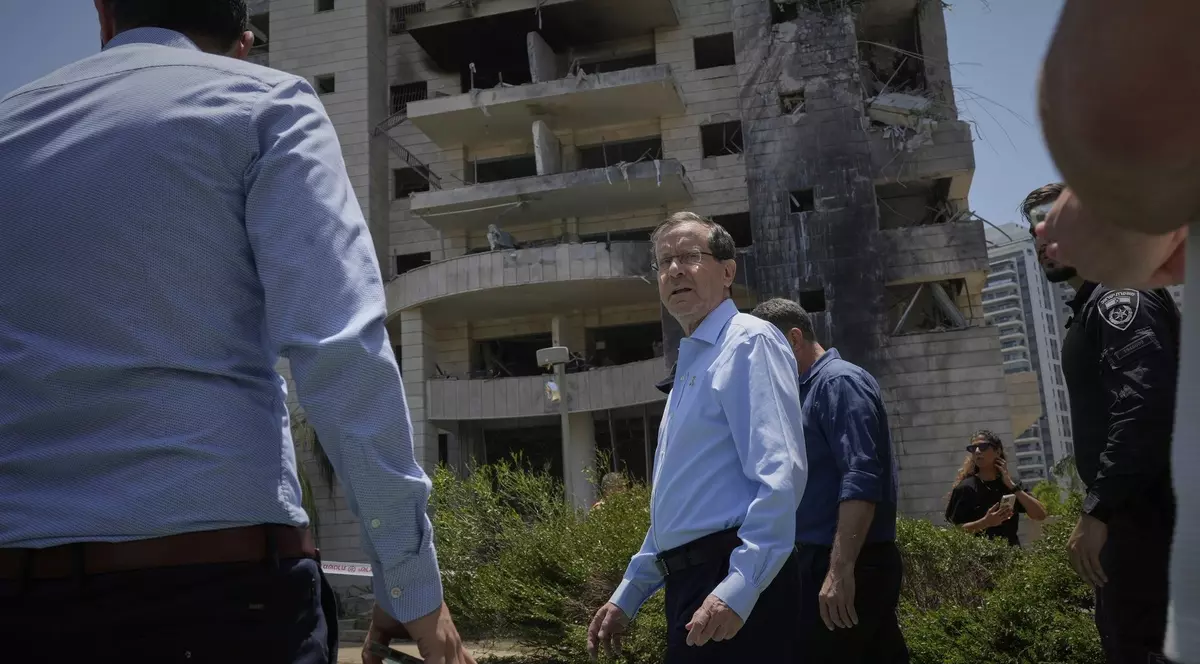 Isaac Herzog surprins în timp ce vizitează o clădire rezidențială lovită de o rachetă lansată din Iran în Petah Tikva, în iunie 2025. Este însoțit de mai mulți oameni