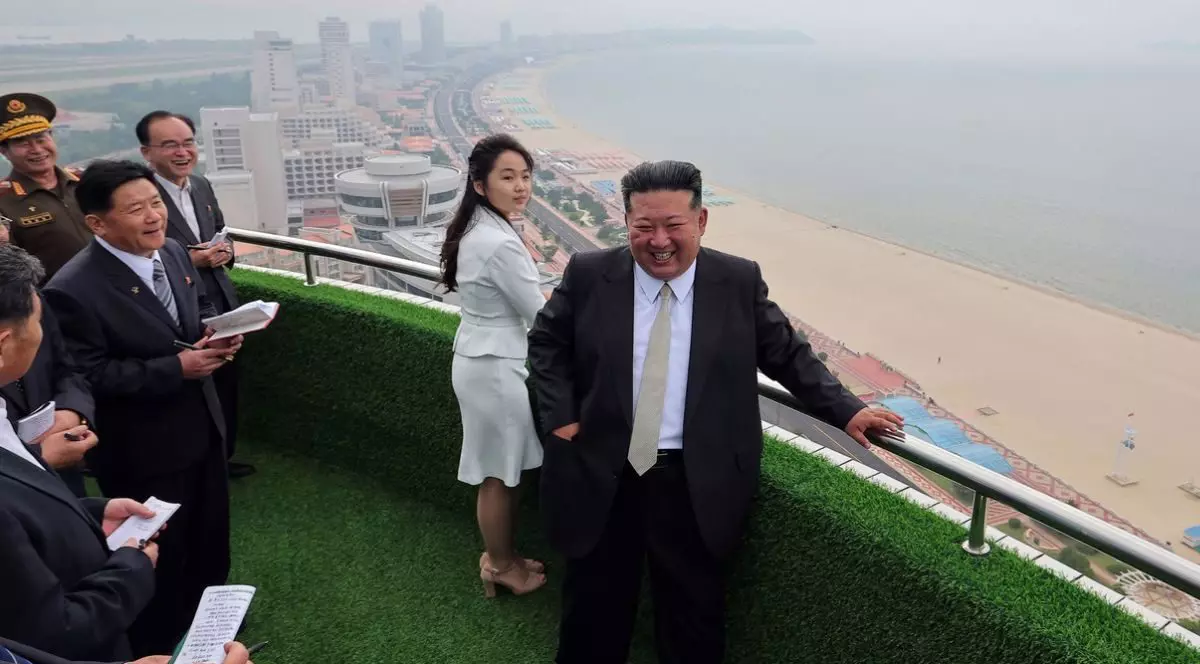 Fotografie publicată de Agenția Centrală de Știri Coreeană îl prezintă pe liderul nord-coreean.Kim Jong-un, în costum negru si camasă albă, și fiica sa, Kim Ju Ae, intr-un deux-piece alb, vizitează zona turistică de coastă Wonsan Kalma, in stanga lor numerosi jurnalisti, in spate se vede plaja si mare intr-o zi cu ceață. 24 iunie 2025