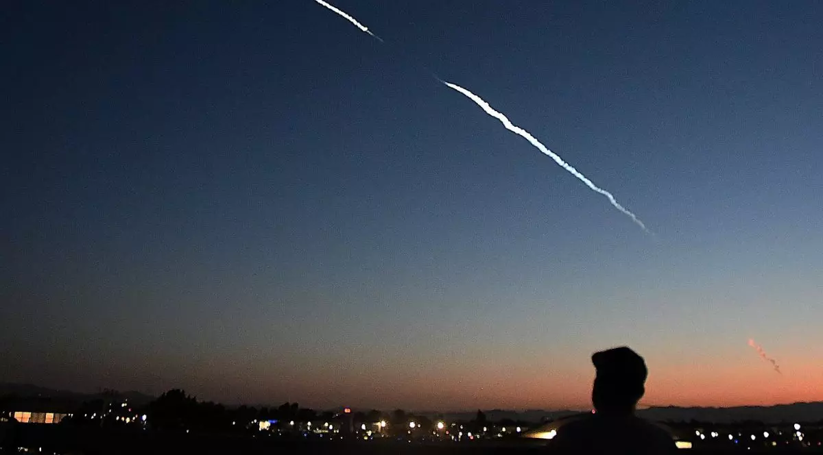 dâră albă de fum văzută pe cer noaptea, în timp ce silueta unui bărbat cu șapcă privește, iunie 2025 - lansare racheta SpaceX