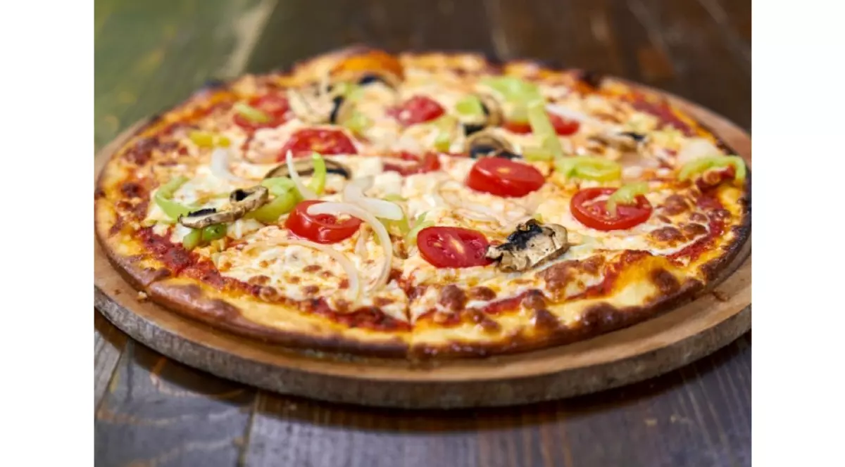 Pizza cu rosii, ardei, ceapa si ciuperci pe o tava de lemn asezata pe masa