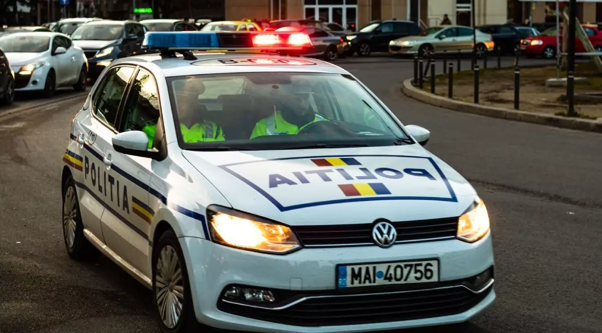 Mașină de Poliție Rutieră, cu girofarul pornit și farurile aprinse, pe o stradă
