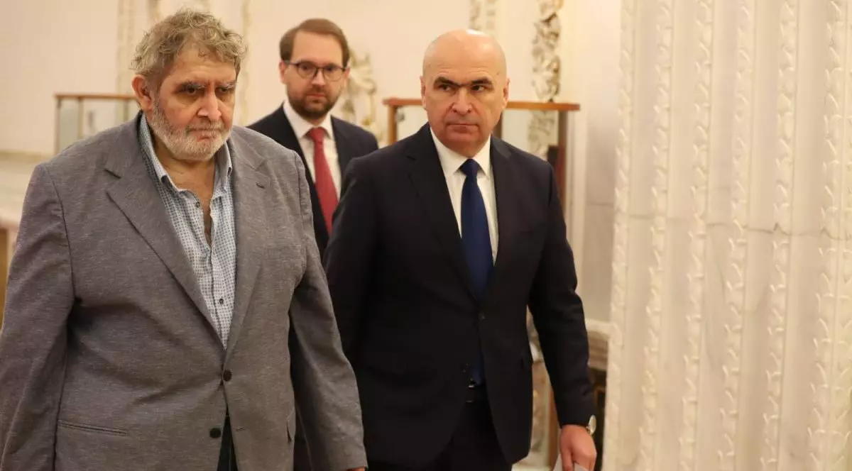 Premierul desemnat Ilie Bolojan merge pe holurile Parlamentului cu un document în mână, lângă el este liderul minorităților alta decât cea maghiară, Varujan Pambuccian, iar în spatele lor este președintele USR, Dominic Fritz, înainte de semnarea programului de guvernare, 23 iunie 2025