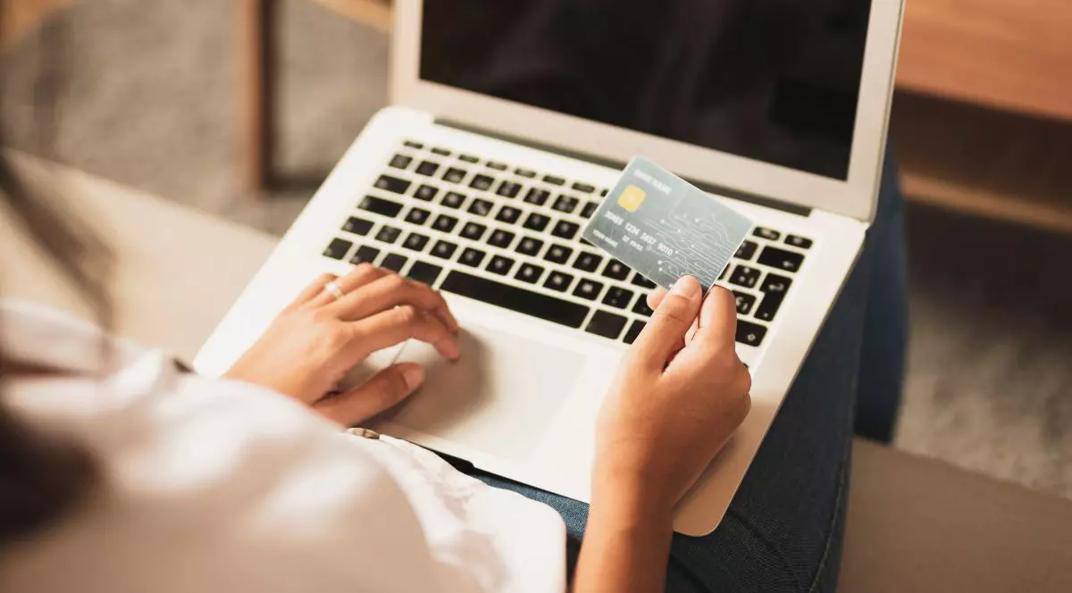 femeie care stă pe laptop și ține în mână un card bancar verde