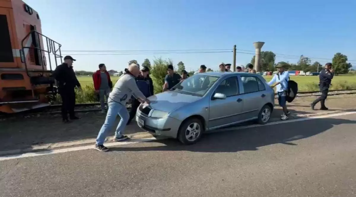 Pasagerii unui tren, la marginea liniei de cale ferată împing o Skoda albastră din fața trenului pentru a elibera drumului locomotivei.