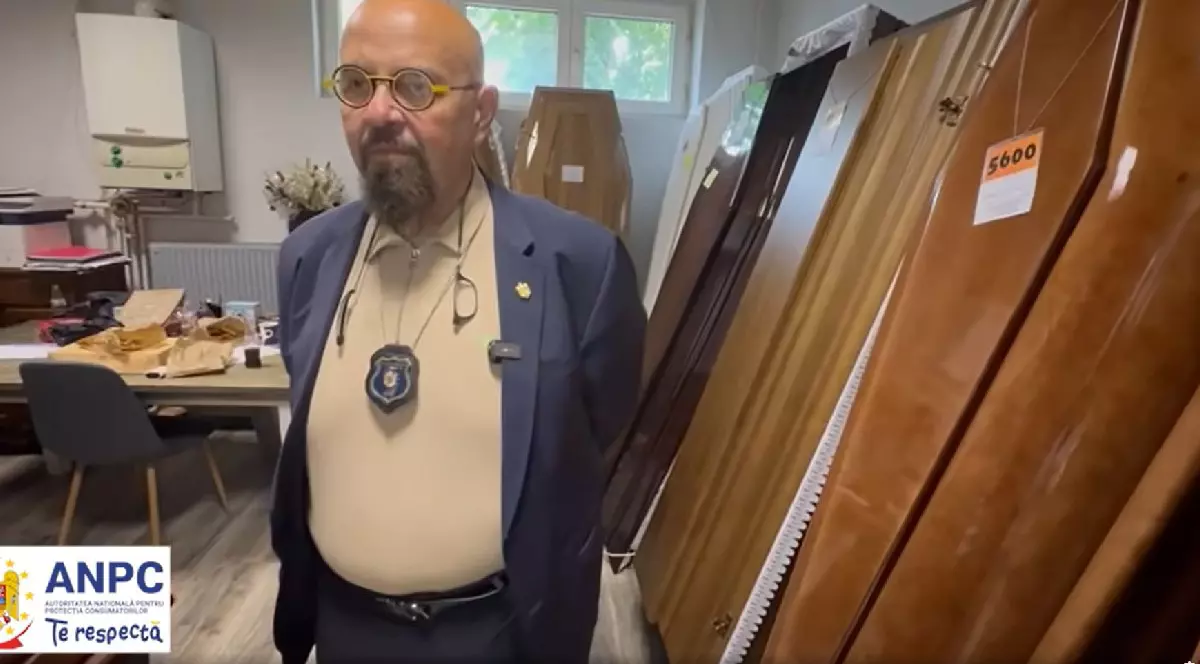 Cristian Popescu Piedone, președintele ANPC, cu tricou bej și sacou bluemarin, ochelari cu ramă galbenă și insigna la gât, stă cu mîinile la spate într-o încăpere în care sunt expuse mai multe sicrie