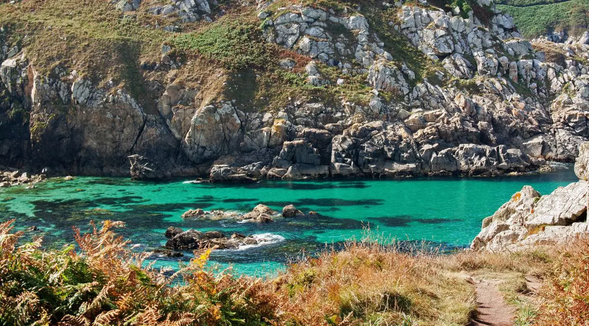 Plaja Cap Coz, o mică lagună cu apă turcoaz, inconjutată de stanci și vegetație verde si arămie