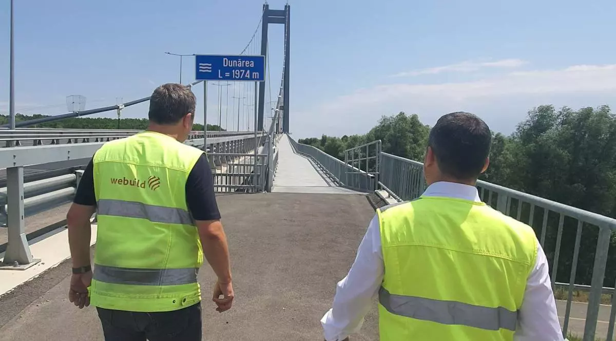 Doi muncitori pe Podul de la Brăila, cei doi poartă veste reflectorizante iar în fața lor se vede lucrarea finalizată