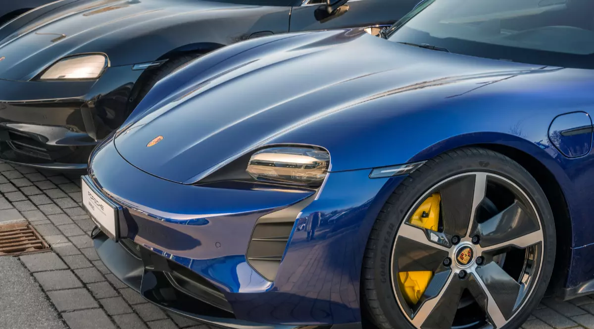 În imagine sunt ilustrate două mașini. Cea din spate este de culoare neagră, iar cea din față este de culoare albastră.