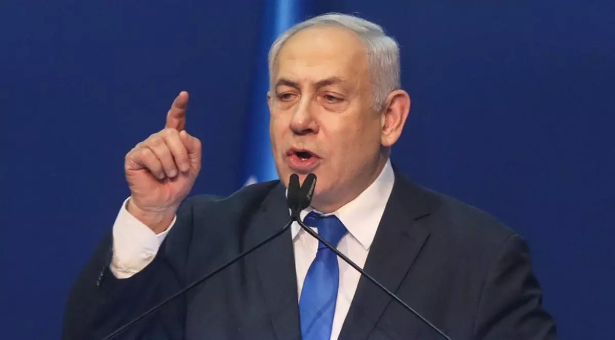 Benjamin Netanyahu, susține un discurs la microfon, purtând un costum bleumarin și o cravată albastră, ținând mâna dreaptă ridicată, cu degetul arătător ridicat