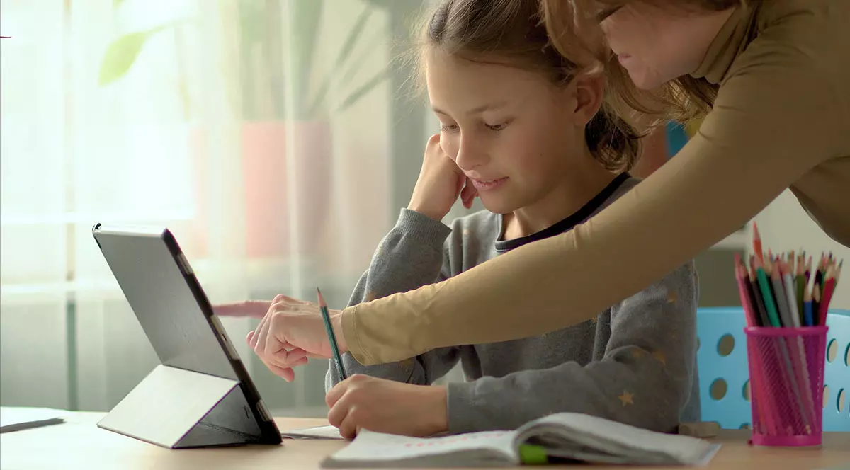 Un fată care învață în sistem homeschooling este ajutată de mama ei la teme