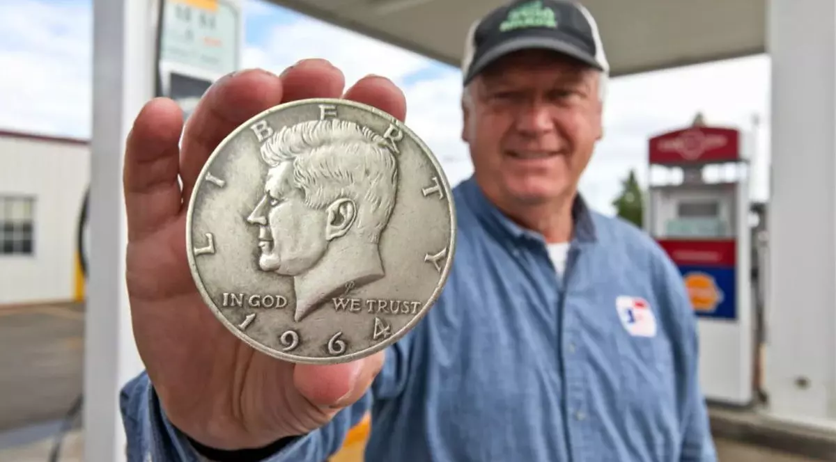 Un bărbat cu șapcă, proprietarul unei benzinării, ține în mână în monedă rară Kennedy Half Dollar, care valorează 3,21 milioane de dolari