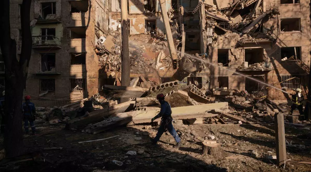 Un soldat ucrainean mergând în fața unui bloc distrus în totalitate de atacurile ruse