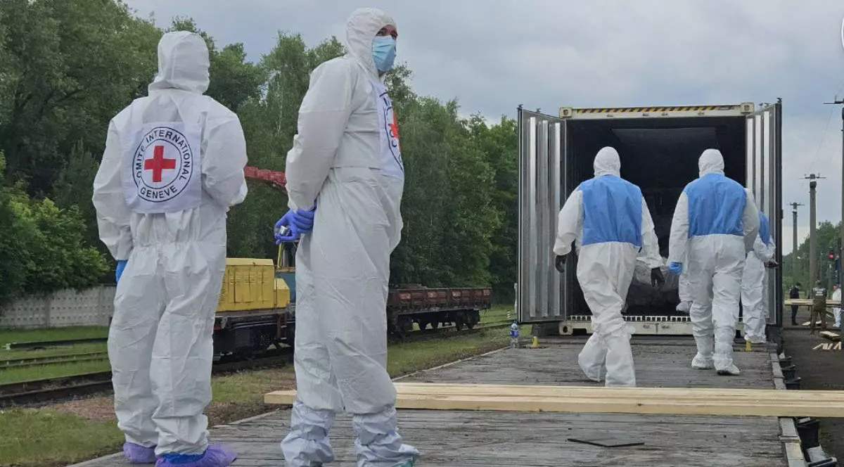 Militari ucraineni îmbrăcați în combinezoane albe așteaptă să ridice cadavrele soldaților morți.