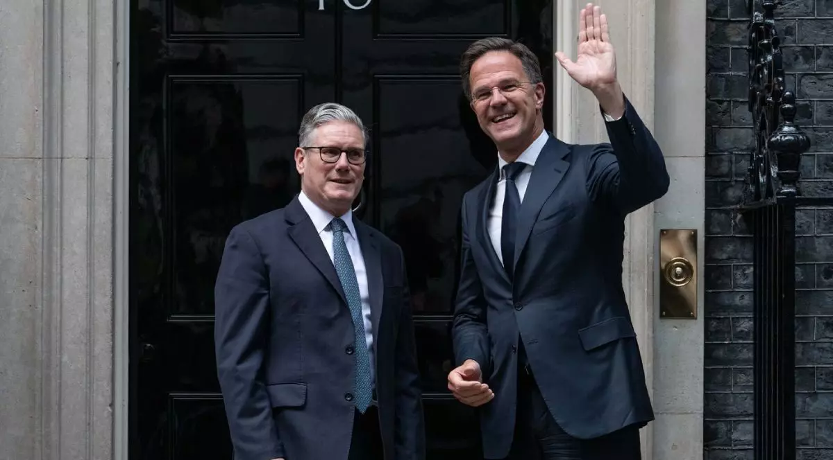 Keir Starmer, stânga, alături de Mark Rutte, cu mana stanga ridicata in semn de salut, dreapta