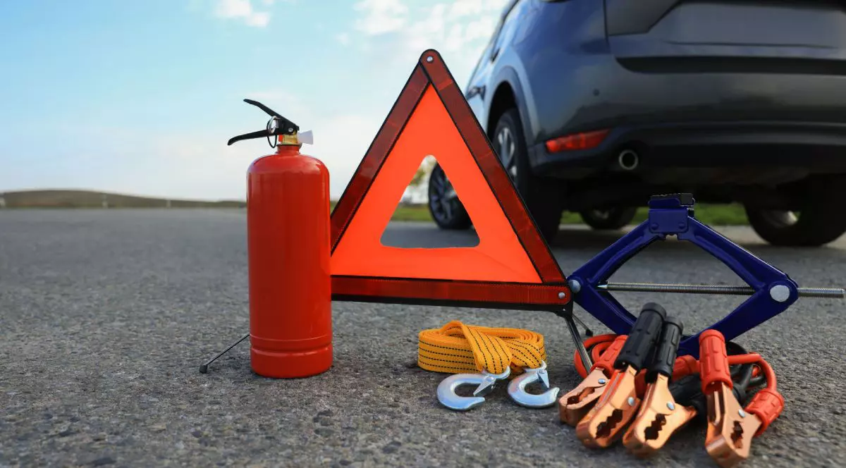 Stingător auto, triunghi reflectorizant, cabluri și cric, pe asfalt, în spatele unei mașini de culoare închisă