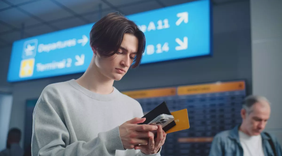 Imagine cu un tânăr în aeroport surprins în timp ce se uită în telefon
