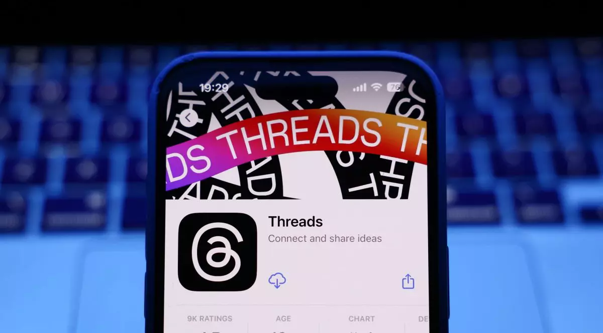 Pagina de pe AppStore a aplicației Threads, deschisă pe un iPhone așezat în fața unei tastaturi de laptop.