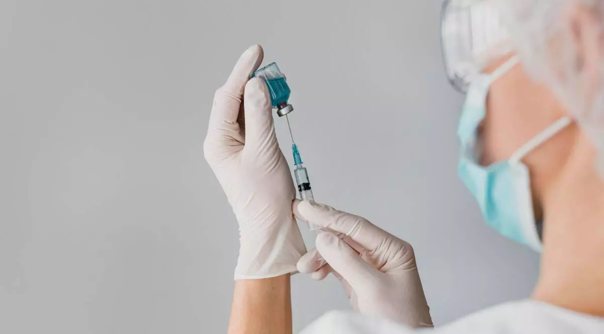 Un doctor în timp ce scoate serul pentru vaccin din fiolă, poartă mască și ochelari de protecție