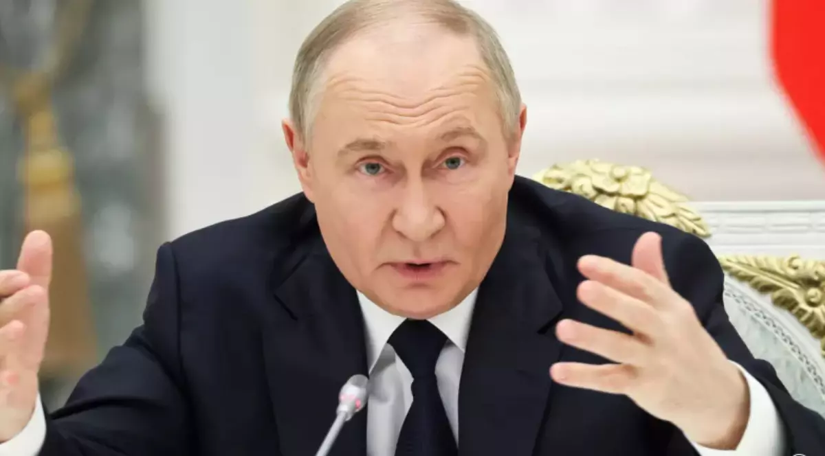 În imagine este ilustrat Vladimir Putin, în costum negru și cămașă albă. Acesta susține un interviu