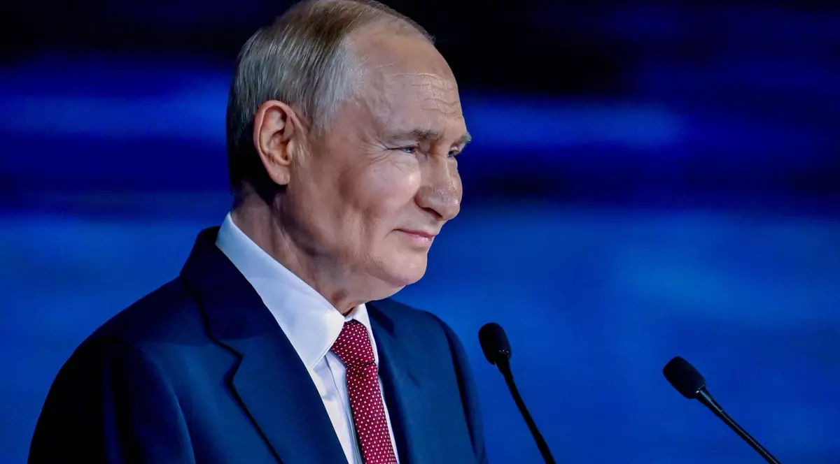 Vladimir Putin a fost surprins zâmbind la Forumul Economic de la Sankt Petersburg, desfășurat în iunie 2025. Liderul rus poartă un sacou albastru, o cravată roșie și o cămașă albă și se află în fața unui microfon
