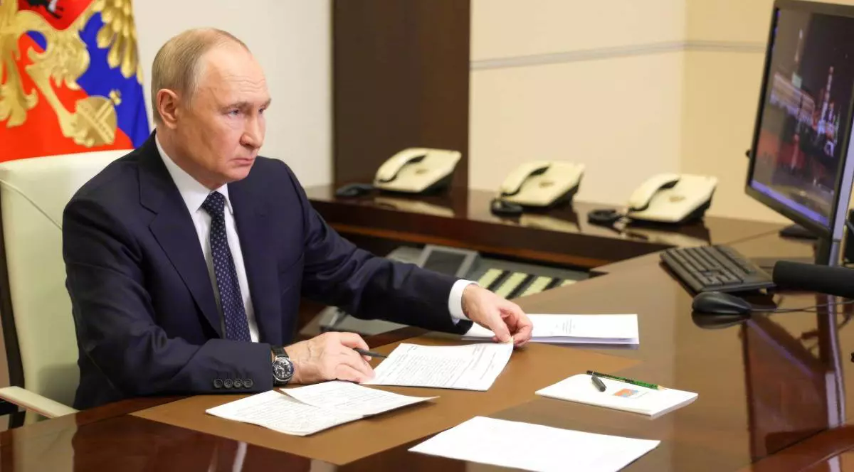 Vladimir Putin în biroul său, stând în fața unui monitor și notând ceva pe o hârtie.