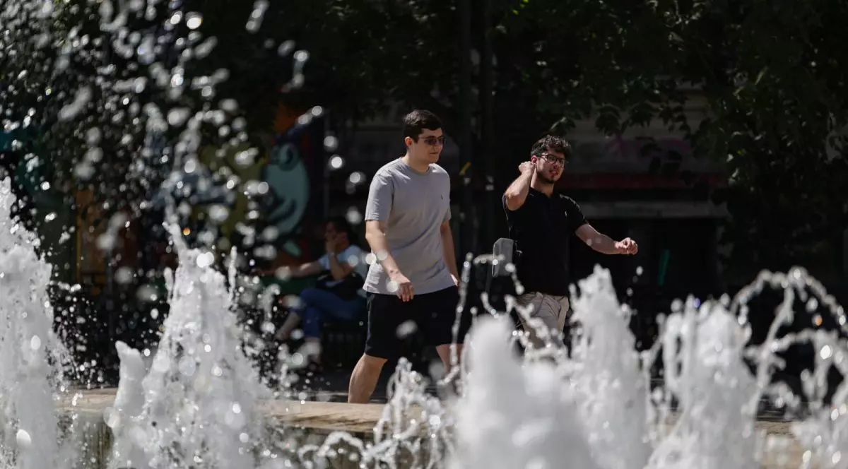 Doi tineri merg pe stradă, în fața lor sunt niște fântâni.