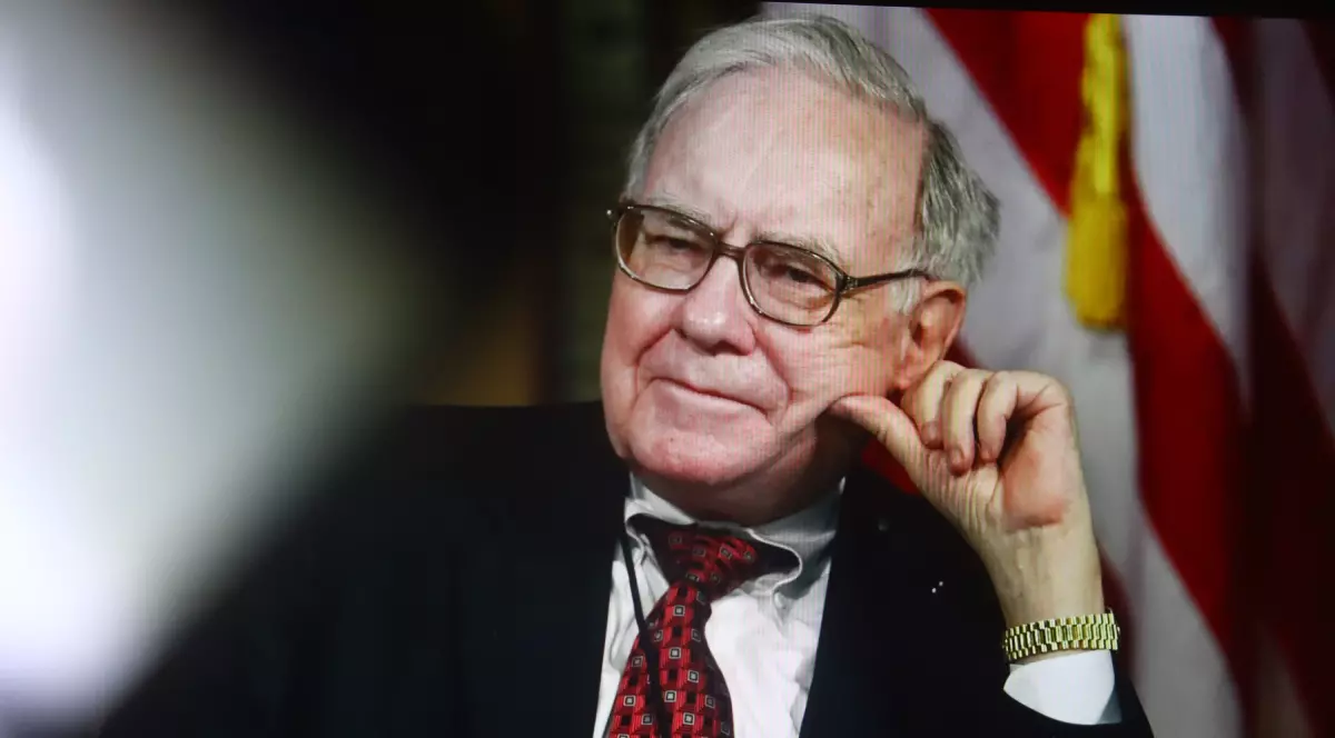 Warren Buffett, îmbrăcat într-un costum negru, cămașă albă și cravată roșie.
