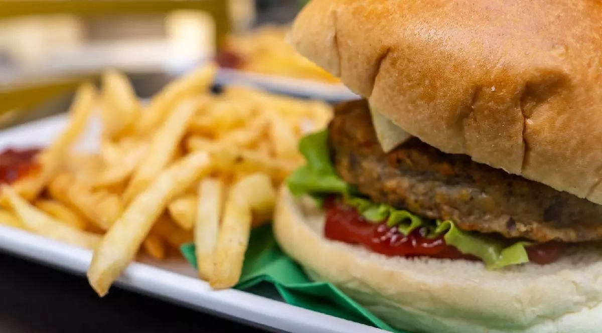 Un burger ;i cartofi pr[ji'i pe o farfurie albă