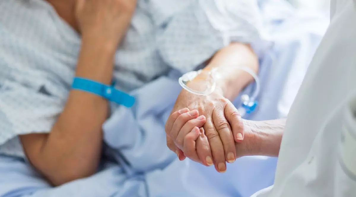 Un doctor ține de mână o femeie care stă într-un pat de spital