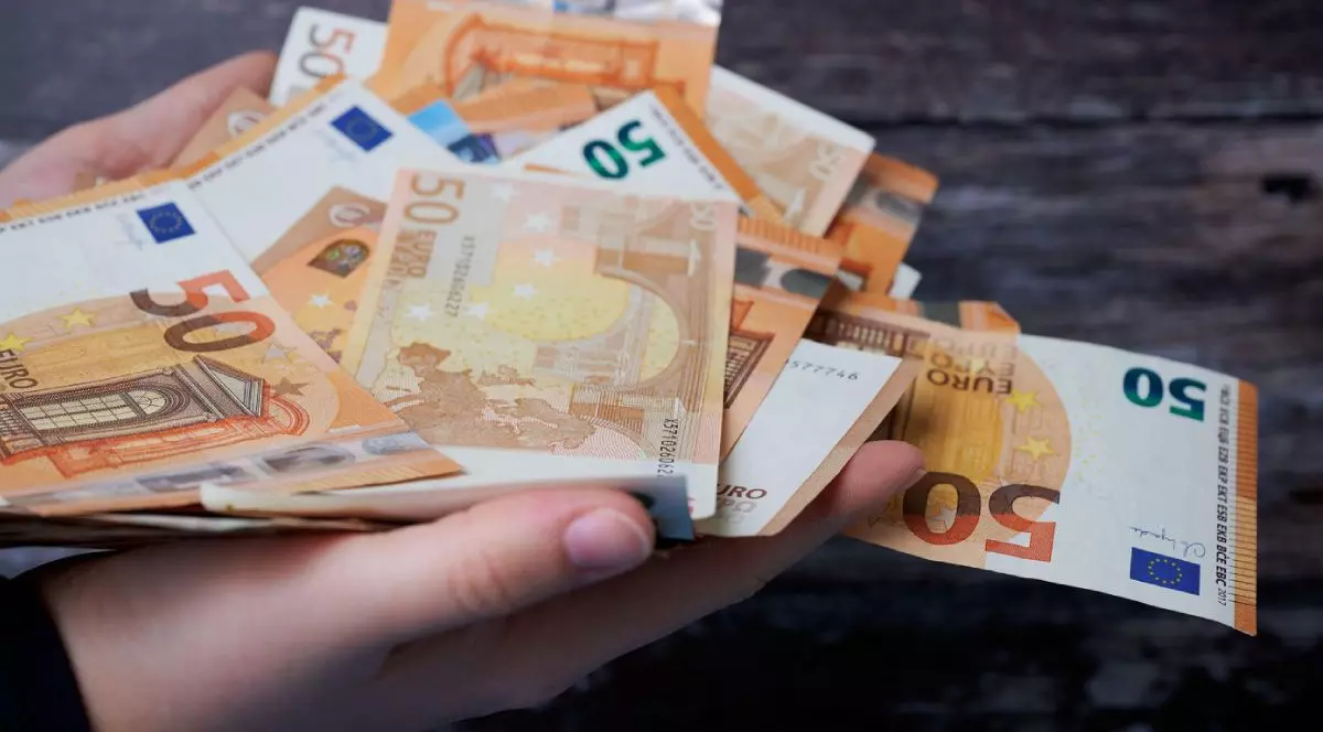 Mai multe bancnote de 50 de euro ținute într-o mână, iar pe fundal se vede lemn de culoare închisă