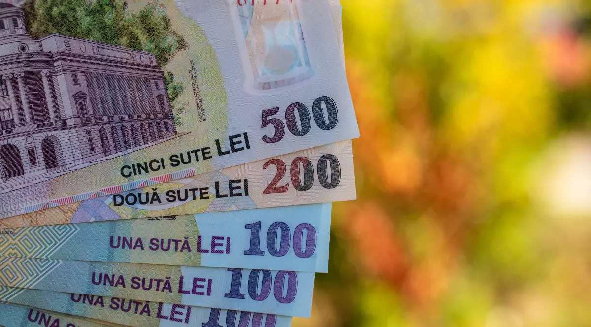 Imaginea prezintă mai multe bancnote românești de diferite valori (500, 200, 100 și 50 de lei), aranjate în evantai, cu un fundal colorat, neclar