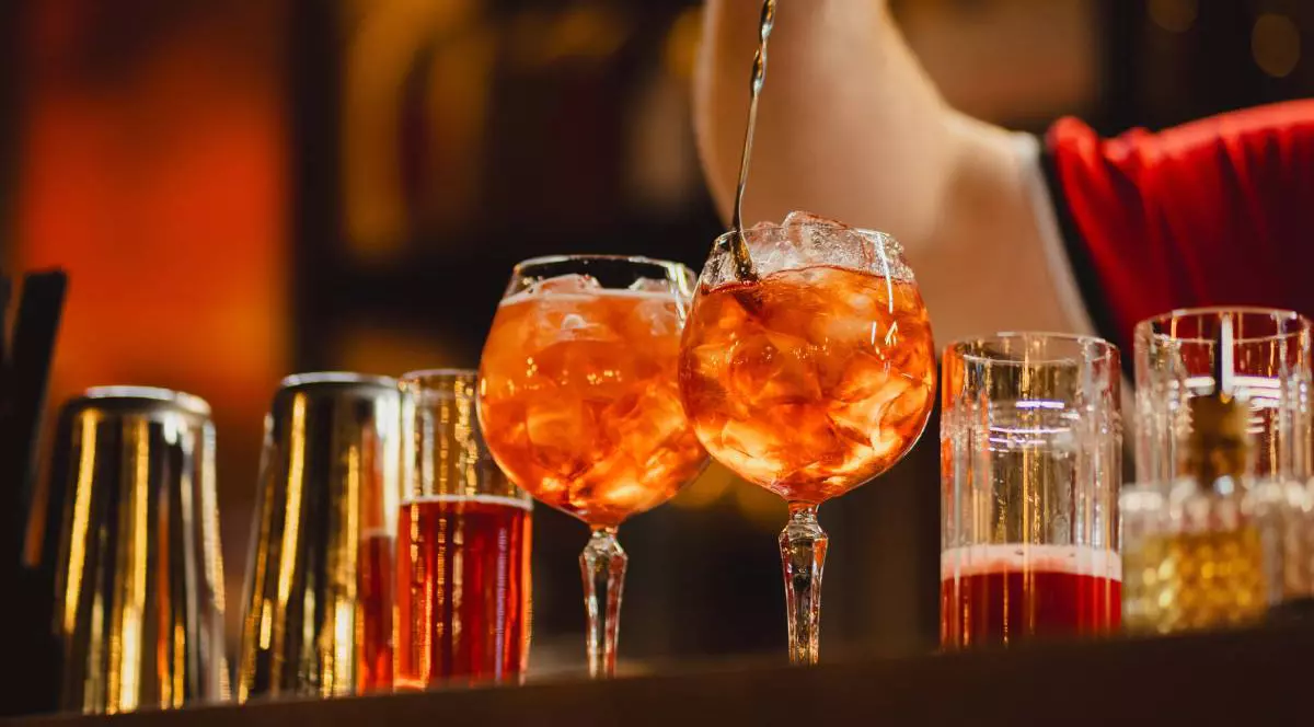 Un barman care pregătește două cockteiluri cu gheață, amestecă în pahar cu o linguriță cu coada foarte lungă
