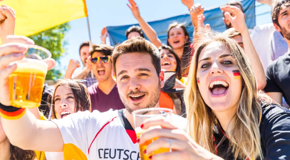 Fani germani care sărbătoresc pe stadion, consumând bere. Grup de suporteri urmărind un meci și susținând echipa națională a Germaniei. Tema combină sportul cu stilul de viață.