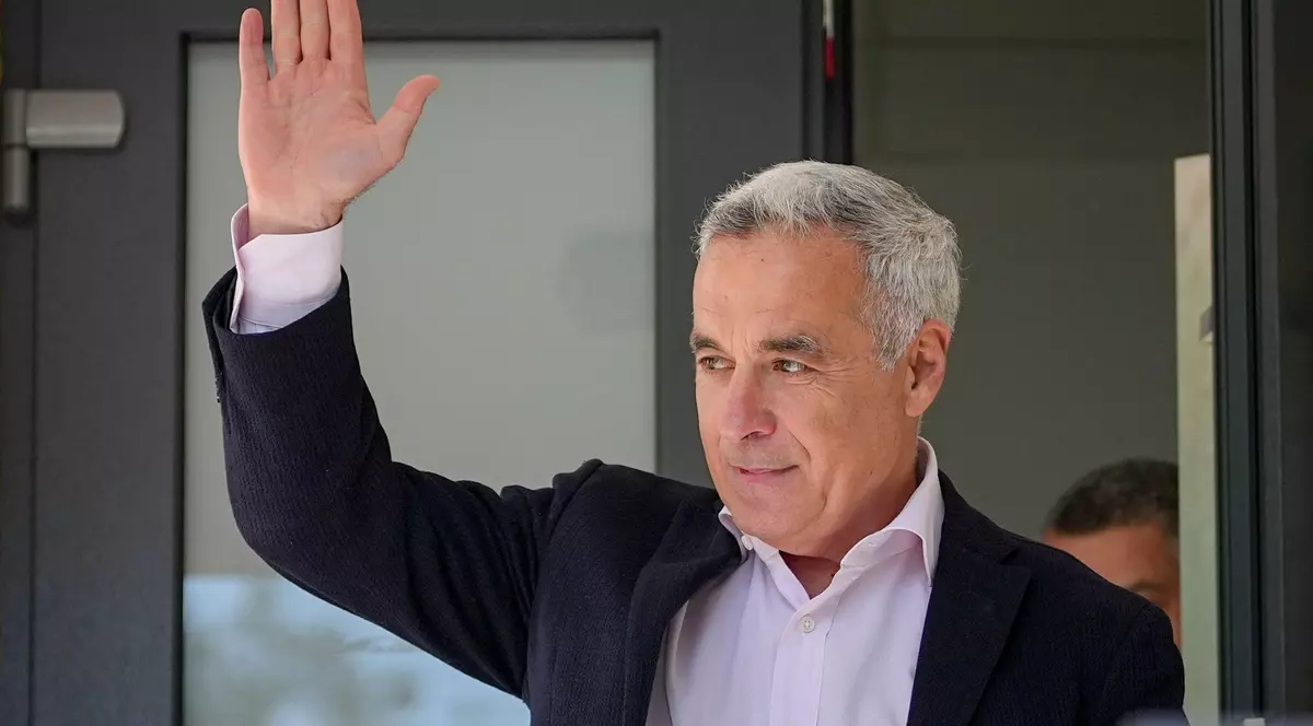 Călin Georgescu surprins cu o mână ridicată în timp ce părăsește sediul IPJ Ilfov, în mai 2025. Poartă un sacou negru și o cămașă roz pudrat