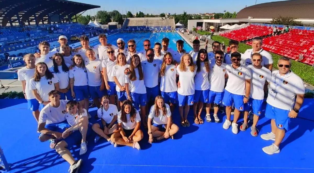 În imagine e echipa de înot a României, juniori, asezați pentru o poză de grup la finalul CAMPIONATELE EUROPENE DE INOT pentru juniori, imbrăcați in tricouri albe si șort albastru, in spatele lor un bazin de inot, - Samorin 1-6.07.2025,
