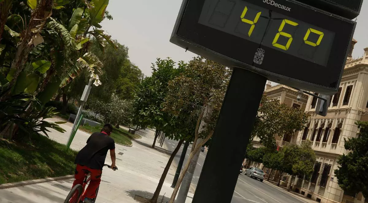 Un bărbat merge cu bicicleta lângă un termometru care marchează 46 de grade în timpul unei zile de alertă roșie