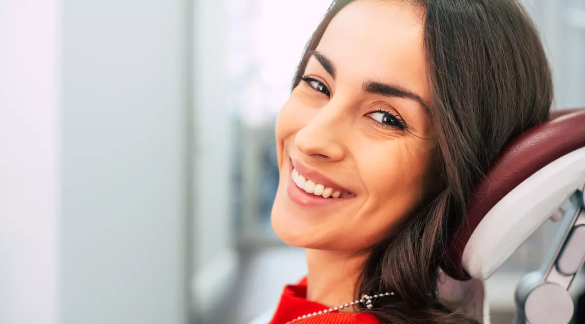 City Dental Clinic - femie satena asezata pe scaunul doctorului dentist, uitandu-se spre camera zambind