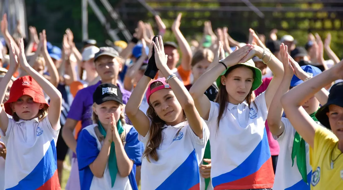 Imagine cu mai mulți copii care au mâinile ridicate și sunt îmbrăcați cu tricouri care au drapelul Rusiei