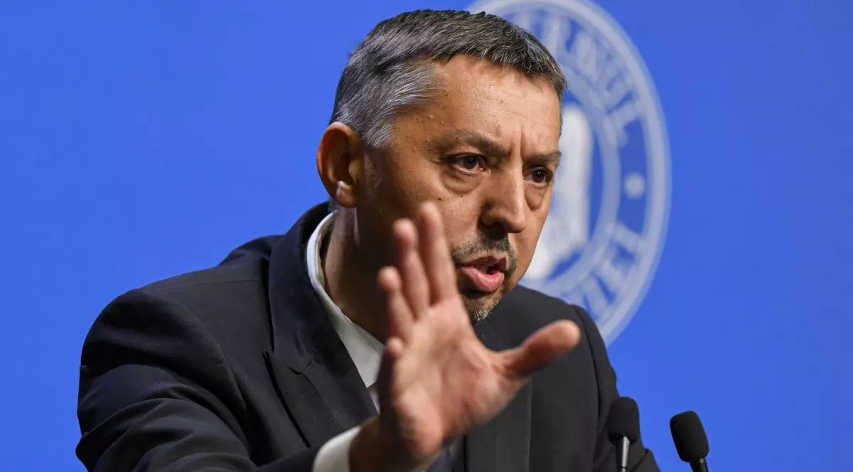 Daniel David, ministrul Educației, îmbrăcat în costum, la pupitrul de la Guvernul României, într-o conferință de presă, cu microfoane în față și logo-ul Guvernului pe fundal albastru în spate