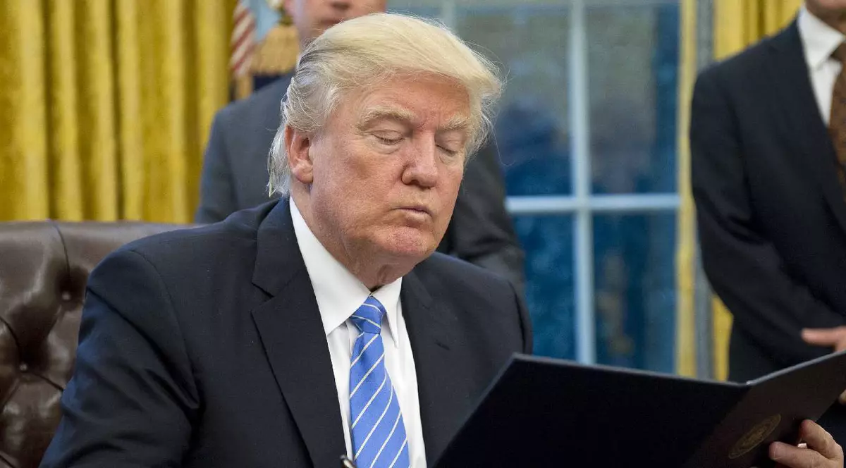 În imagine, Donald Trump citește ceva așezat la biroul de la Casa Albă