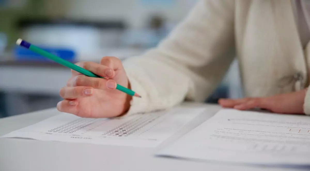 Elev care scrie cu creionul pe o foaie de hârtie la examen