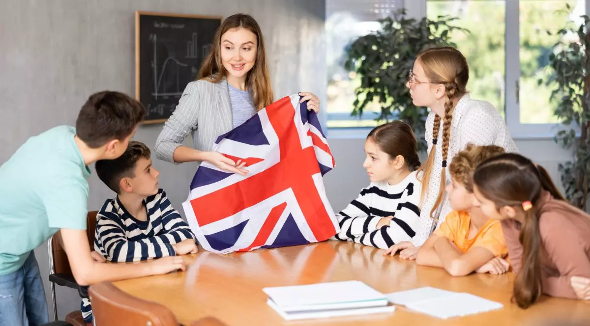 Elevi din Marea Britanie în clasă alături de profesoara care ține un steag