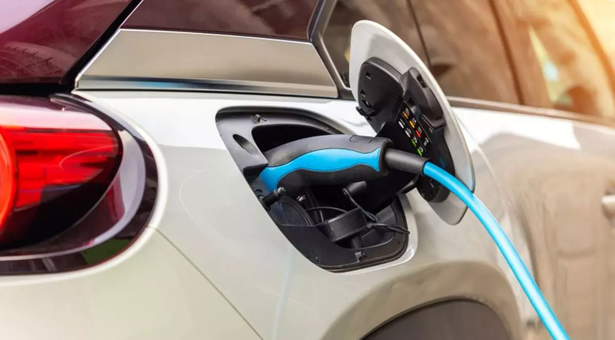 Prim-plan cu o mașină hibridă electrică modernă, parcată lângă stația de încărcare rapidă pe strada centrală a unui oraș european vechi.