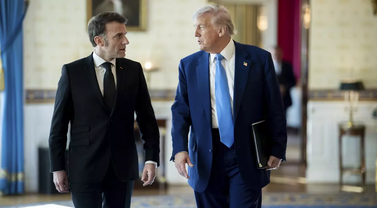 Emmanuel Macron (stânga) și Donald Trump (dreapta) surprinși în timp ce vorbesc. Președintele francez poartă un costum negru, cu o cămașă albă și cravată neagră, iar președintele SUA poartă unul albastru. Liderul american are cămașă albă și o cravată albastru deschis. Imaginea a fost făcută în februarie 2025